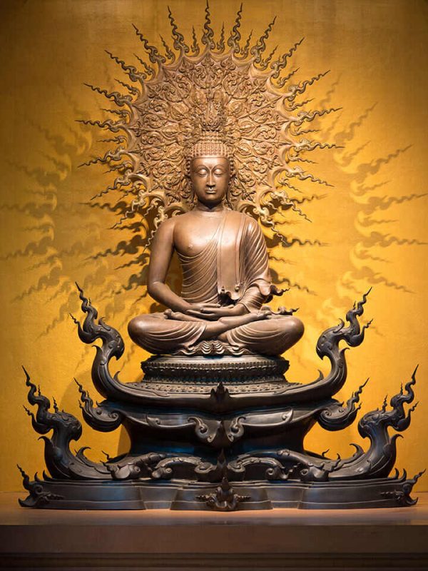 Golden Buddha sculpture in lotus position sitting on an orange background - Image 2